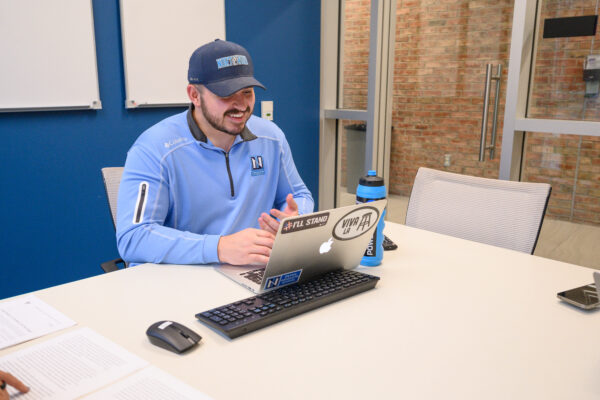 Graduate student in Northwood apparel using his laptop and smiling