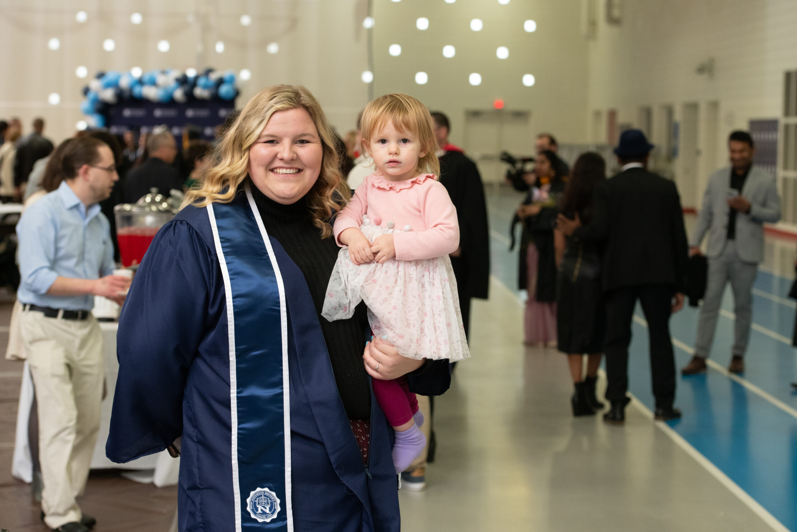 Northwood Online student holding her baby in her cap and gown attire