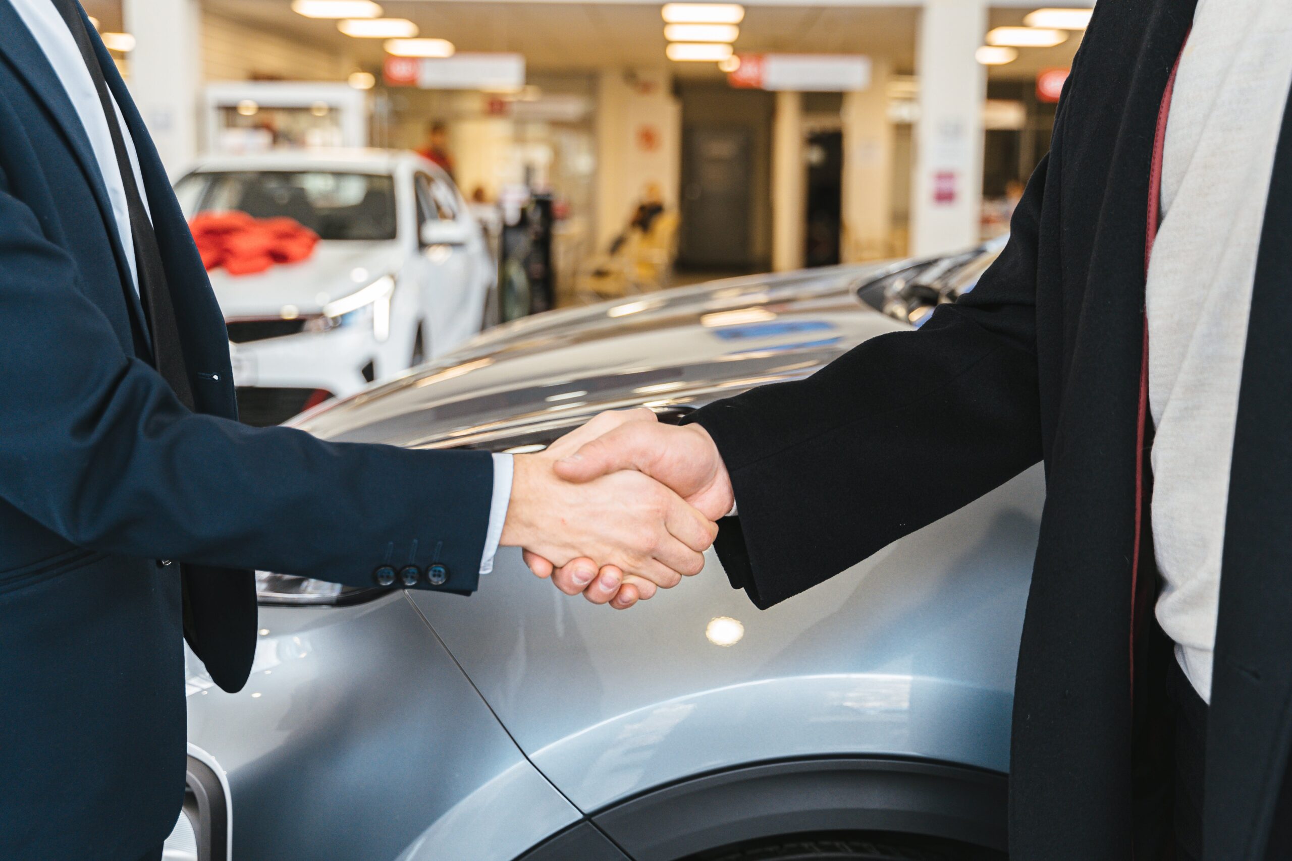 Man in a suit shaking the hand of another man with a car behind them